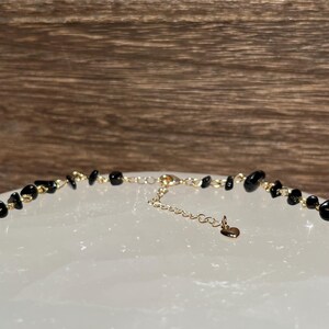 May include: A black gemstone necklace with a gold chain and a heart charm.