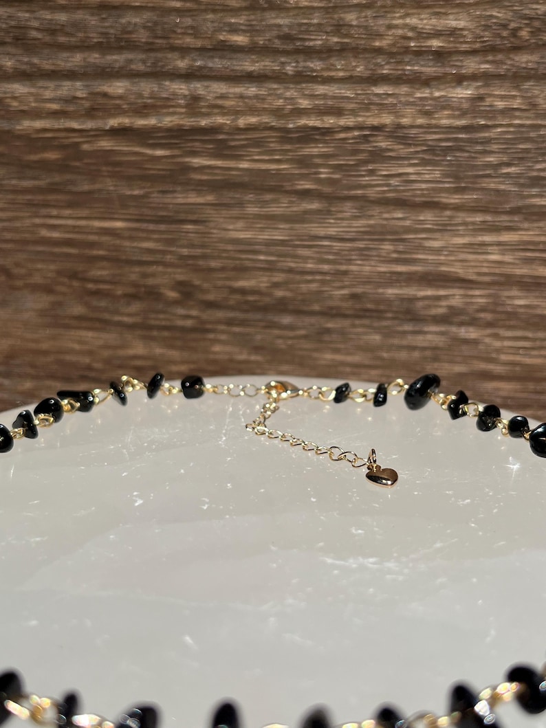 May include: A black gemstone necklace with a gold chain and a heart charm.