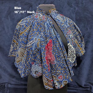 Puede incluir: Capa de batik azul, cuello de 16"/17" (aprox. 41-43 cm). Presenta un vibrante estampado de motivos florales y aves en rojo, blanco y amarillo sobre fondo azul oscuro. Cuello alto y dise&ntilde;o suelto.