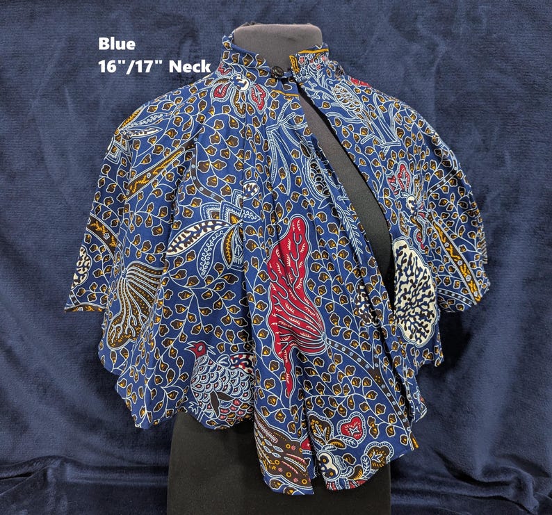 Puede incluir: Capa de batik azul, cuello de 16"/17" (aprox. 41-43 cm). Presenta un vibrante estampado de motivos florales y aves en rojo, blanco y amarillo sobre fondo azul oscuro. Cuello alto y dise&ntilde;o suelto.