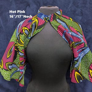 Puede incluir: Una capa rosa intenso estampada con cuello de 40.6cm/43.2cm. La capa presenta un dise&ntilde;o vibrante con detalles en rosa, amarillo, verde y azul sobre un fondo negro. La prenda se exhibe en un maniqu&iacute; negro.
