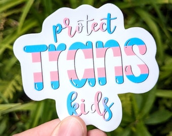 May include: A white sticker with the words "protect TRANS kids" in blue and pink lettering. The word "TRANS" is filled with the colors of the transgender flag: light blue, pink, and white stripes. The sticker has a cloud-like shape.