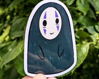 May include: A sticker featuring a character from the animated film Spirited Away. The character has a white face with black eyes and purple markings, and is wearing a dark teal robe. The sticker has a white border.