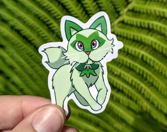 May include: A sticker featuring a cartoon cat with light green fur, green accents, and pink eyes. The cat has a white muzzle and whiskers, and a green bow tie. The sticker is held against a backdrop of green fern leaves.