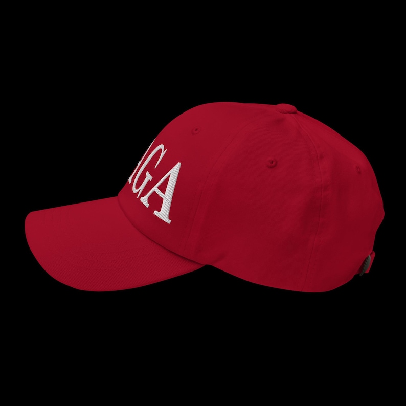 Op de afbeelding: Een rode baseballpet met de wit geborduurde letters "GA" op de voorkant. De pet heeft een gebogen klep en een verstelbare band aan de achterkant. De achtergrond is zwart.