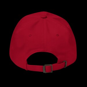 Op de afbeelding: Effen rode baseballcap met een gebogen klep. De achterkant heeft een verstelbare metalen gespsluiting voor een pasvorm op maat. De cap is gemaakt van een zachte, duurzame stof.