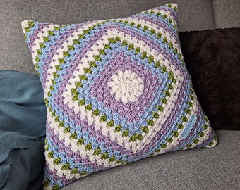 Könnte beinhalten: Ein gehäkeltes Kissen mit einem quadratischen Muster in den Farben Grün, Lila, Blau und Weiß. Das Kissen ist mit einem Granny-Square-Stich gearbeitet.
