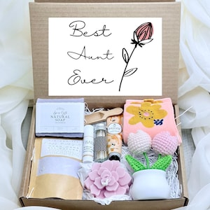 May include: A gift box containing a bar of natural soap, a small wooden scoop, a lip balm, a glass vial of matches, a tube of honey hand cream, a pink flower-shaped candle, and two crocheted tulips in a white pot, with a Best Aunt Ever card.