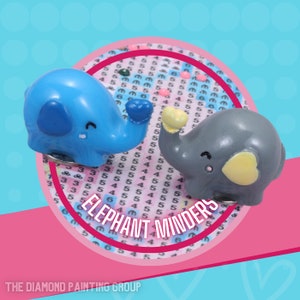 May include: Two small elephant figurines, one blue and one gray, are holding hearts. The figurines are on a diamond painting canvas with the words "Elephant Minders" printed on it.