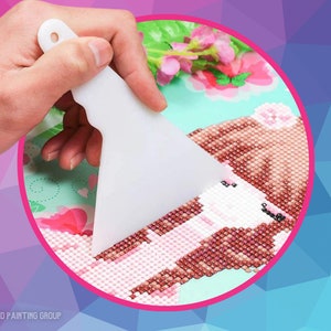 May include: A white plastic tool with a rounded edge is used to press down on a diamond painting of a girl with brown hair and a pink dress. The painting is set against a light blue background with pink flowers.