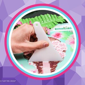 May include: A white plastic tool with a triangular shape is used to press down on diamond painting. The tool is held in a hand and is being used to press down on a diamond painting.