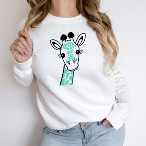 Puede incluir: Sudadera blanca con una ilustraci&oacute;n de jirafa de color turquesa y negro.