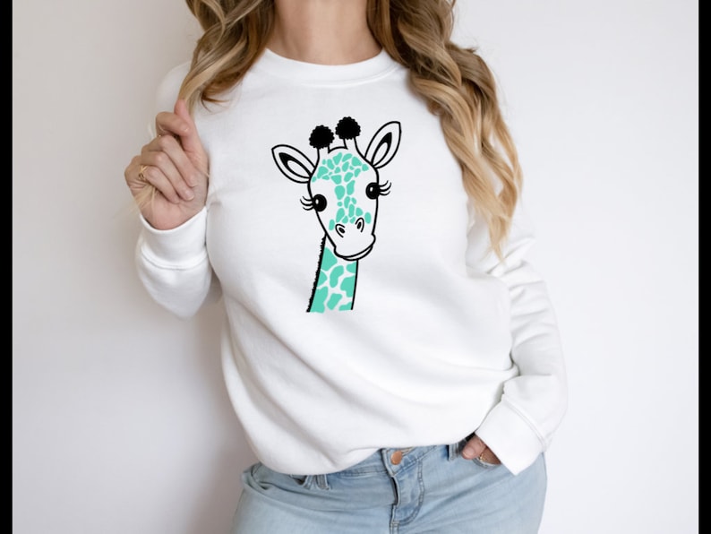 Puede incluir: Sudadera blanca con una ilustraci&oacute;n de jirafa de color turquesa y negro.