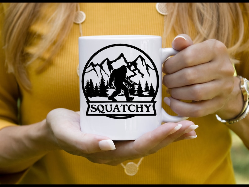 May include: White ceramic mug with a black silhouette of Bigfoot in a mountain landscape. The text "SQUATCHY" is printed below the image.
