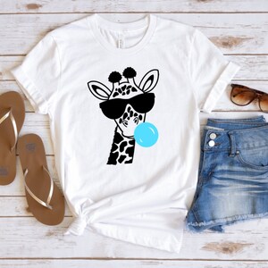 Puede incluir: Camiseta blanca con una ilustraci&oacute;n en blanco y negro de una jirafa con gafas de sol y soplando una burbuja azul.