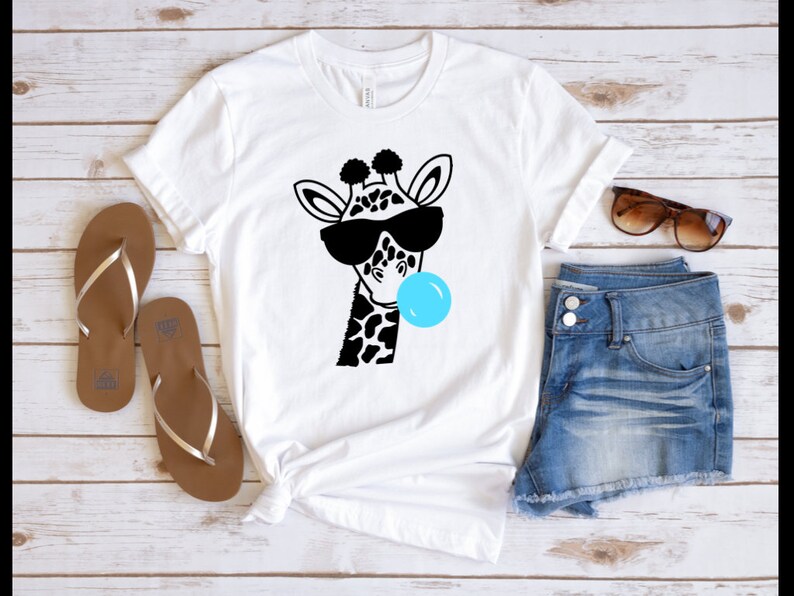 Puede incluir: Camiseta blanca con una ilustraci&oacute;n en blanco y negro de una jirafa con gafas de sol y soplando una burbuja azul.