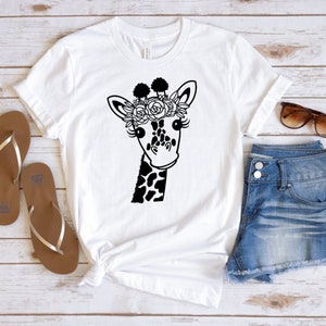 Puede incluir: Camiseta blanca con una ilustraci&oacute;n en blanco y negro de una jirafa con una corona de flores.