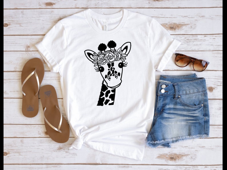 Puede incluir: Camiseta blanca con una ilustraci&oacute;n en blanco y negro de una jirafa con una corona de flores.