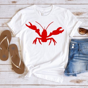 K&ouml;nnte beinhalten: Wei&szlig;es T-Shirt mit einem roten Hummer-Silhouetten-Motiv. Das Shirt wird mit Jeans-Shorts und braunen Flip-Flops kombiniert.
