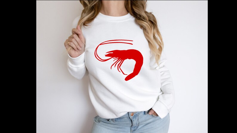 K&ouml;nnte beinhalten: Wei&szlig;er Pullover mit einem roten Garnelen-Motiv.