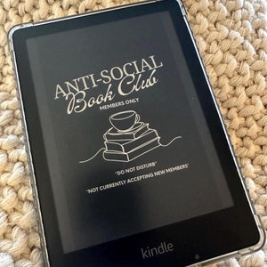 May include: A black and white image on a Kindle e-reader screen that says "ANTI-SOCIAL Book Club" with a stack of books and a coffee cup illustration. The text below says "MEMBERS ONLY" and "DO NOT DISTURB" and "NOT CURRENTLY ACCEPTING NEW MEMBERS".