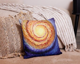 May include: A square throw pillow featuring a vibrant, painterly depiction of a spiral galaxy. The center glows with bright yellow and orange hues, swirling outward into deep purple and blue tones, accented by small white dots representing stars.
