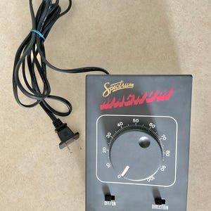 May include: A grey Spectrum Magnum power control unit featuring a large circular dial with numbered settings from 0 to 100, two black toggle switches labeled OFF/ON and DIRECTION, and an attached black electrical power cord with a two-prong plug.