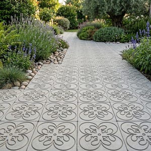 May include: A paved pathway with a floral pattern leads through a lush garden. The pathway is made of gray concrete tiles. The garden features various green plants, lavender, and small rocks along the edges, creating a serene outdoor space.