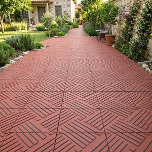 May include: Red brick patio tiles with a geometric pattern create a pathway. The tiles are laid in a repeating design, leading towards a stone building and lush greenery. Potted plants and trees line the sides.
