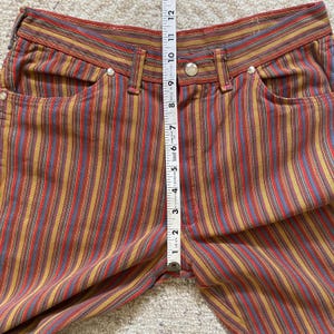 K&ouml;nnte beinhalten: Mehrfarbige gestreifte Hose mit einem roten, blauen, gelben und braunen Farbmuster. Die Hose hat eine hohe Taille und eine lockere Passform.