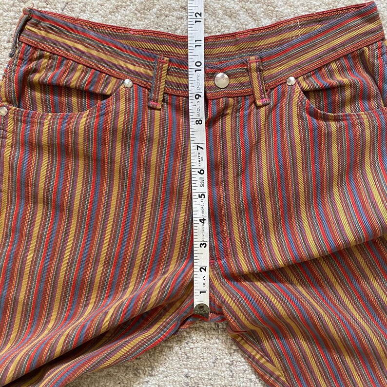K&ouml;nnte beinhalten: Mehrfarbige gestreifte Hose mit einem roten, blauen, gelben und braunen Farbmuster. Die Hose hat eine hohe Taille und eine lockere Passform.