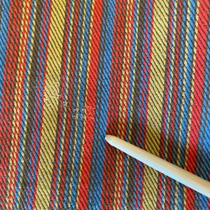 K&ouml;nnte beinhalten: Nahaufnahme eines gestreiften Stoffes mit abwechselnden B&auml;ndern in Rot, Blau, Gelb und Braun. Der Stoff hat eine gewebte Textur.