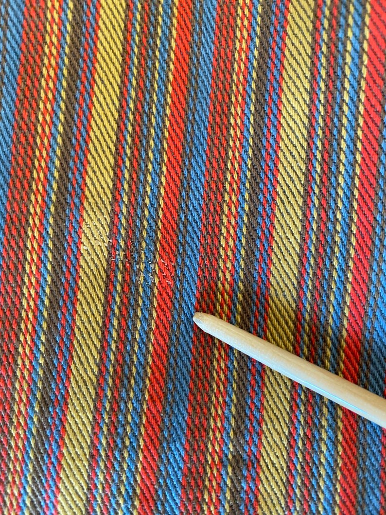 K&ouml;nnte beinhalten: Nahaufnahme eines gestreiften Stoffes mit abwechselnden B&auml;ndern in Rot, Blau, Gelb und Braun. Der Stoff hat eine gewebte Textur.