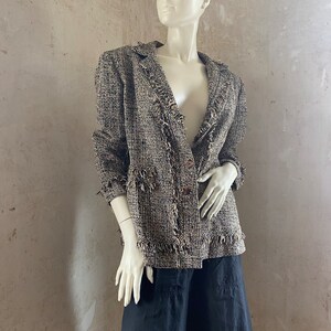 Könnte beinhalten: Eine braune und schwarze Tweedjacke mit Fransenbesatz. Die Jacke hat einen V-Ausschnitt und einen einzigen Knopfverschluss.