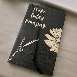 May include: Black leather journal with a gold embossed daisy and the text "Make Today Amazing".