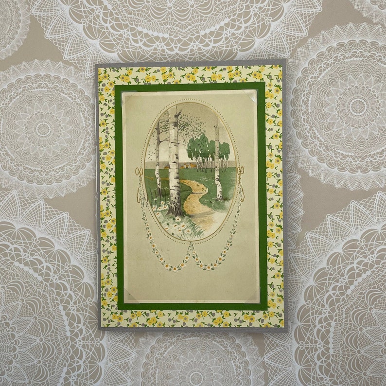 Puede incluir: Una tarjeta de felicitaci&oacute;n vintage con un borde floral verde, amarillo y blanco. La tarjeta presenta una imagen de un camino que conduce a trav&eacute;s de un bosque de abedules.