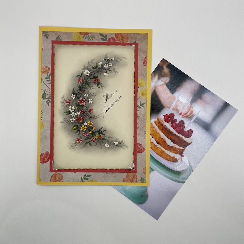 May include: A yellow card with a red border and a floral design. The card has the text "heureux anniversaire" written on it.
