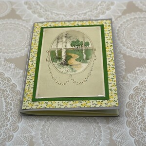 Puede incluir: Una tarjeta de estilo vintage con un borde floral verde y amarillo. La tarjeta presenta una imagen de un camino a trav&eacute;s de un bosque con abedules y una peque&ntilde;a casa en la distancia.