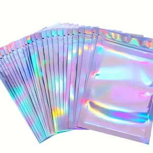 May include: A stack of iridescent holographic zip-top bags. The bags are a light purple color with a rainbow sheen.