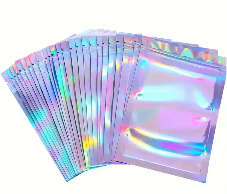 May include: A stack of iridescent holographic zip-top bags. The bags are a light purple color with a rainbow sheen.