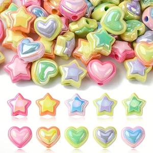 May include: A collection of colorful, iridescent beads in star and heart shapes. The beads are in shades of pink, yellow, green, and blue. The beads have a glossy finish and are arranged in a pile.