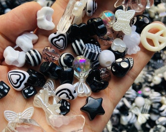 May include: A selection of black and white plastic beads, including hearts, stars, bows, dice, and peace signs. The beads are held in a hand, with many more beads visible in the background.
