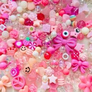 May include: A large assortment of pink and white beads, charms, and other decorative elements. The beads are made of various materials, including plastic, glass, and metal. Some of the charms include hearts, stars, flowers, and bows. The beads and charms are perfect for making jewelry, keychains, or other crafts.