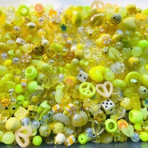 May include: A large assortment of yellow and lime green plastic beads in various shapes, including hearts, stars, peace signs, and fruit slices.