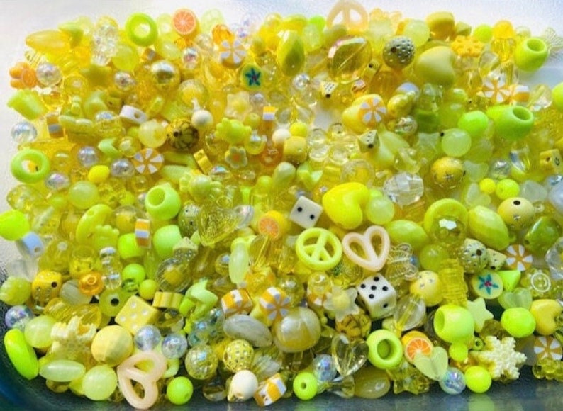 May include: A large assortment of yellow and lime green plastic beads in various shapes, including hearts, stars, peace signs, and fruit slices.
