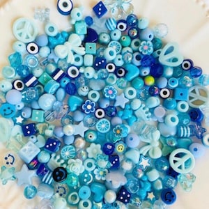 May include: A large assortment of blue and white plastic beads in various shapes, including stars, flowers, peace signs, hearts, and more. The beads are perfect for making jewelry or other crafts.