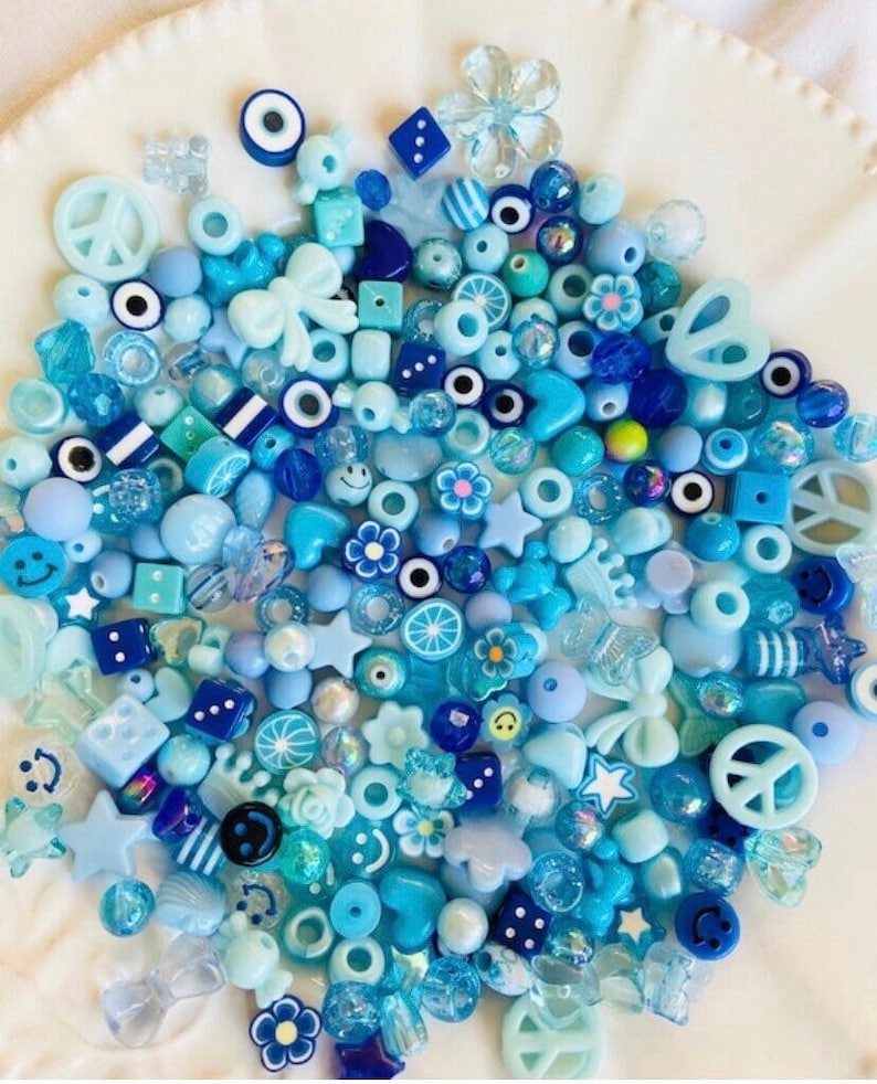 May include: A large assortment of blue and white plastic beads in various shapes, including stars, flowers, peace signs, hearts, and more. The beads are perfect for making jewelry or other crafts.