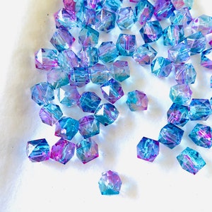 May include: A scattering of iridescent blue and purple glass beads, each with a faceted hexagonal shape.