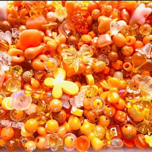 May include: A large assortment of orange and yellow plastic beads, including hearts, flowers, butterflies, and bows. The beads are perfect for crafting jewelry or other decorative items.