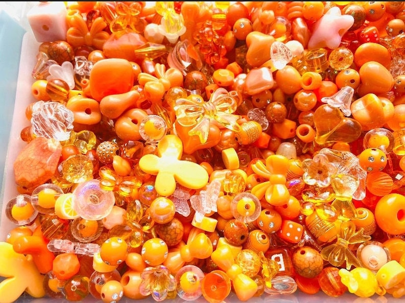 May include: A large assortment of orange and yellow plastic beads, including hearts, flowers, butterflies, and bows. The beads are perfect for crafting jewelry or other decorative items.